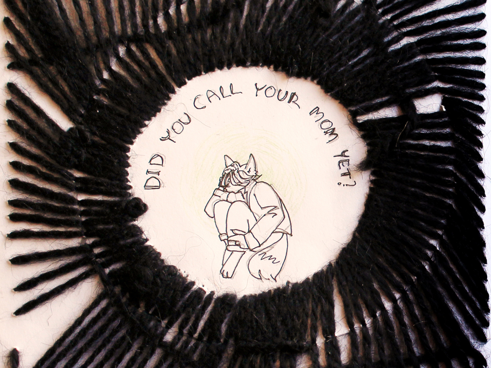 A photo of a thick black embroidery on paper. The embroidery radiates out in the shape of a circle. In the center of the circle is drawn a curled up figure with fox ears and a tail, under a text reading 'did you call your mom yet?'